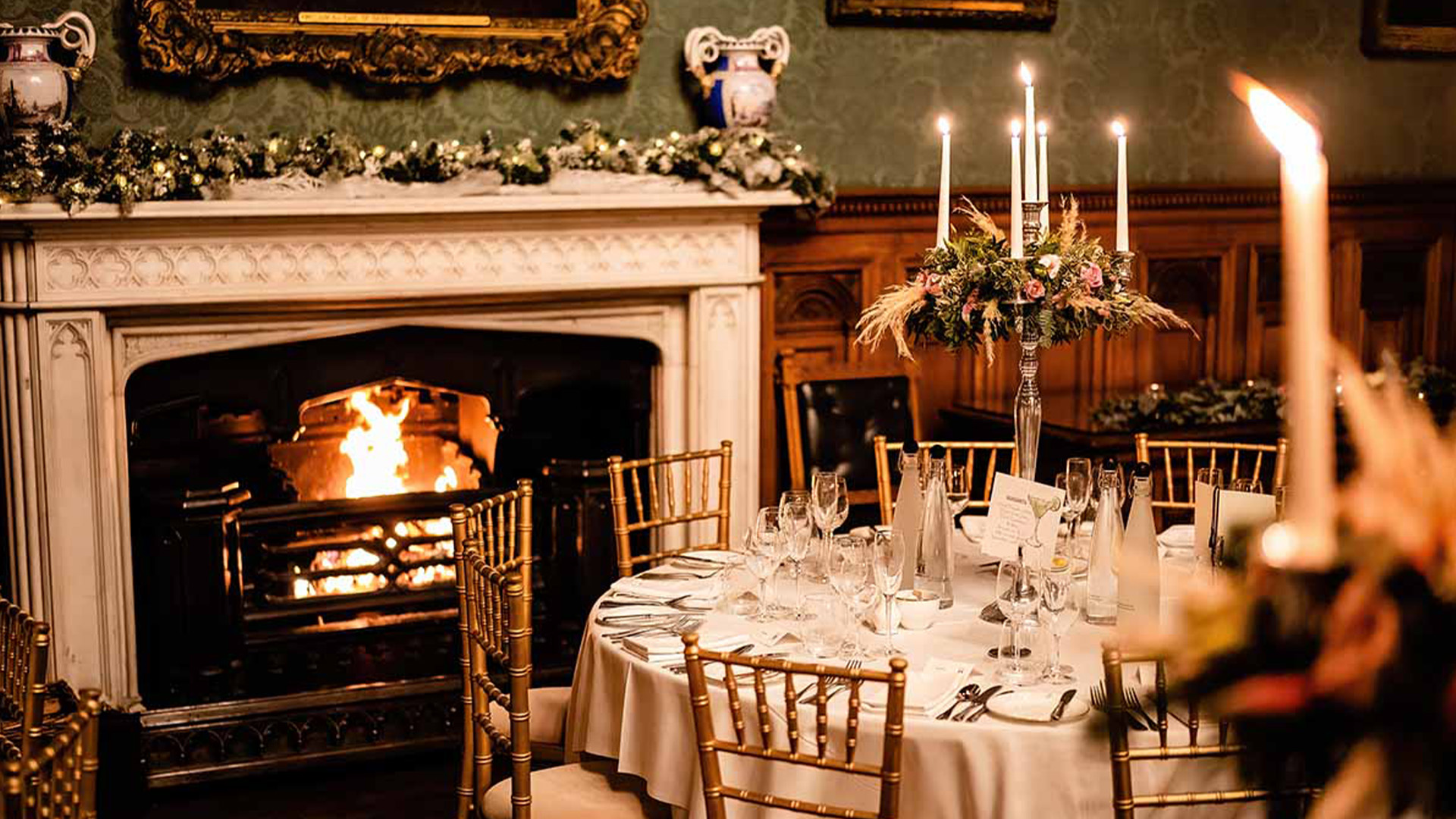 A dining room set for a Christmas wedding breakfast with a roaring open fire, Christmas garland above fireplace and table and chairs