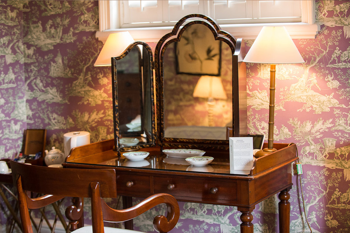 Close up angle view of a wooden dressing table with mirror and chair and chair. Surrounded by a pink mural wallpaper