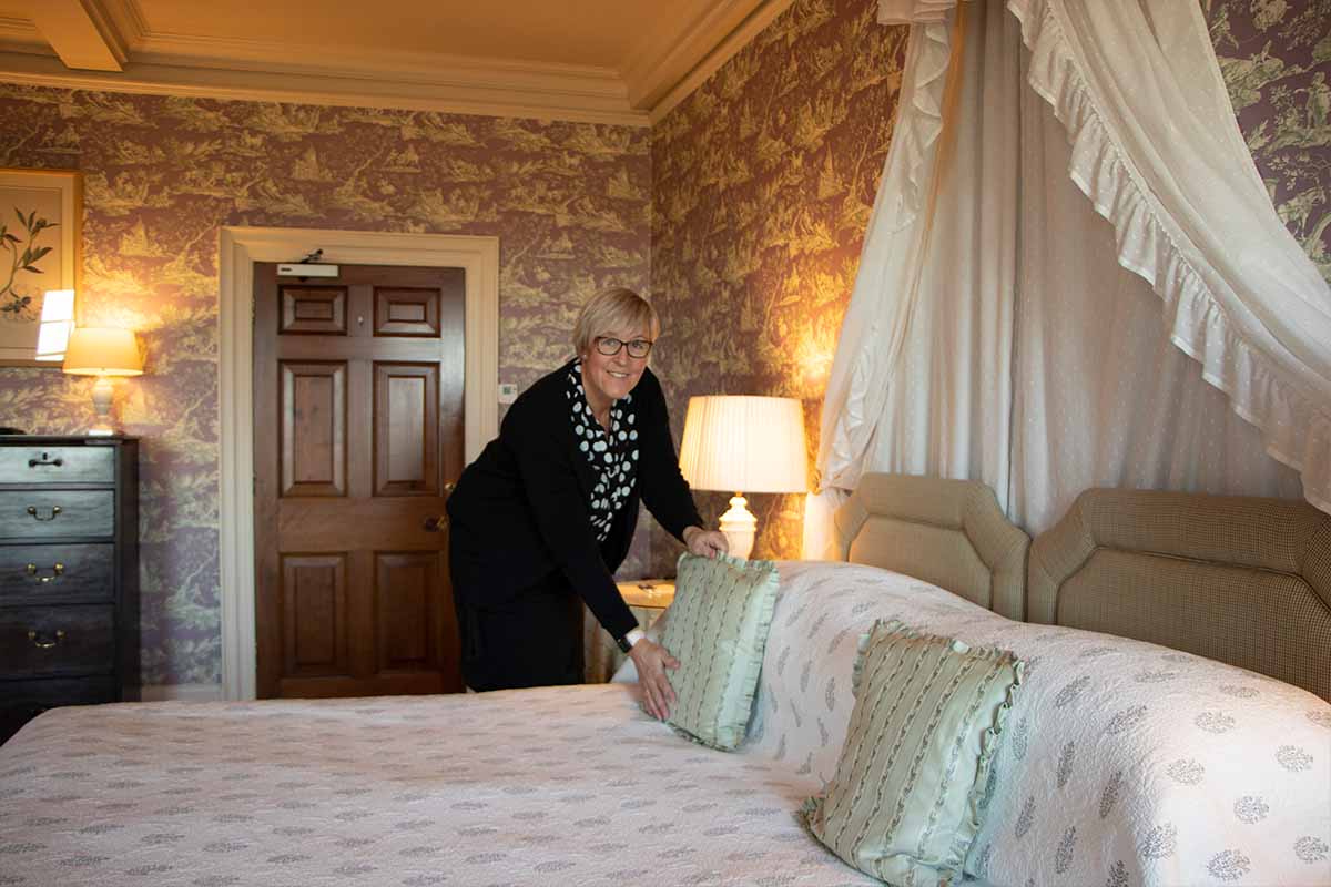 Housekeeper in bedroom placing cushions on bed at Knowsley Hall