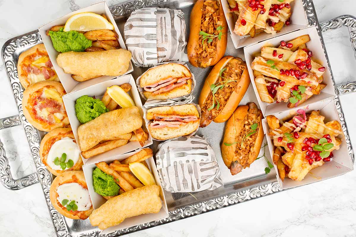 A silver tray filled with a selection of food with pizzas, fish and chips, sausages and bacon rolls