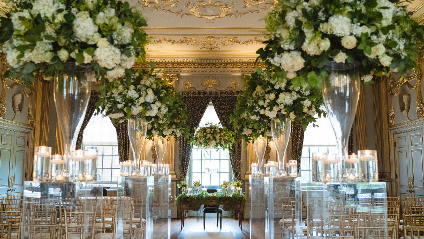 A stunning room filled with beautiful fresh flowers and chairs set for a wedding ceremony